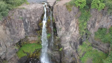drone fly above a amazing waterfall in the middle of the wild nature with lush green forest in iceland