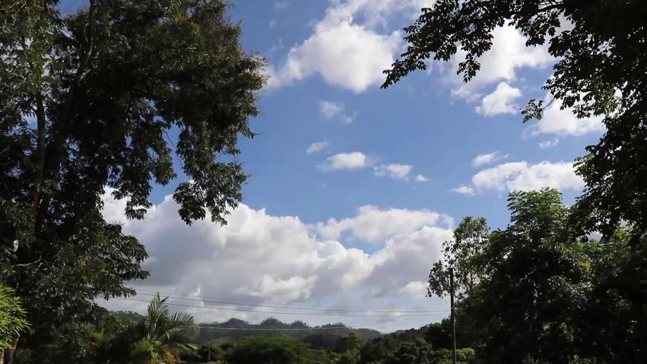 Timelapse clip of puffy white clouds moving across a blue sky in Honduras. Mountains in the background.