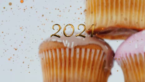 Animation-of-2021-over-cupcakes-on-white-background