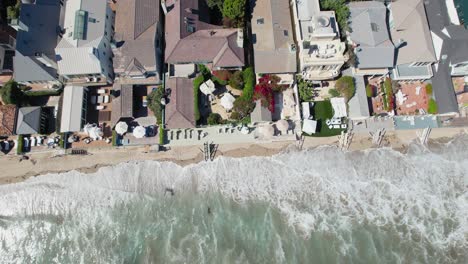 pacific ocean waves almost hitting luxury homes in malibu, aerial top down view