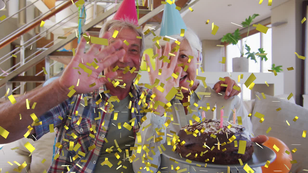 feliz pareja de adultos mayores caucásicos en sombreros de fiesta haciendo video llamada de cumpleaños con pastel y confeti de oro