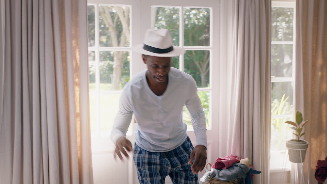 funny african american man dancing in bedroom having fun celebrating feeling positive enjoying successful lifestyle doing silly dance at home on weekend morning wearing pajamas