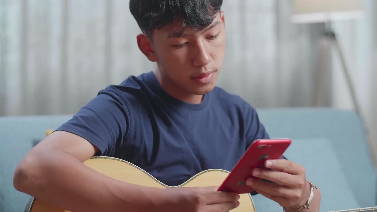 스마트폰을 보고 집에서 기타를 연주하는 노트북을 가진 아시아 소년 작곡가의 클로즈업