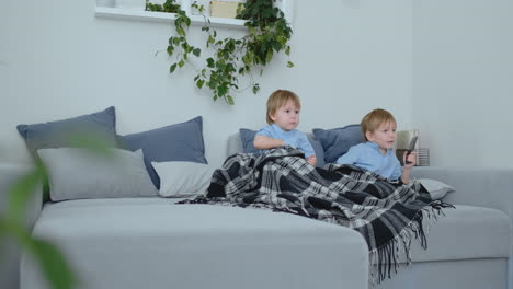 Two-boys,-4-and-2-years-old,-are-watching-TV-sitting-on-the-couch.-An-exciting-TV-show.-View-cartoons.-Children-watch-an-exciting-TV-show.