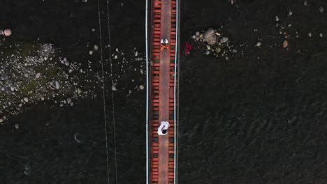 Man-And-Woman-In-Traditional-Cable-Bridge-With-Serene-Stream-Waters-Flowing-Below--Guinsaugon,-Southern-Leyte,-Philippines