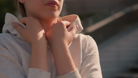 close-up of woman gently touching her hoodie collar, hands crossed and resting on her neck, creating a warm and reflective moment, soft sunlight highlights her skin and casual attire