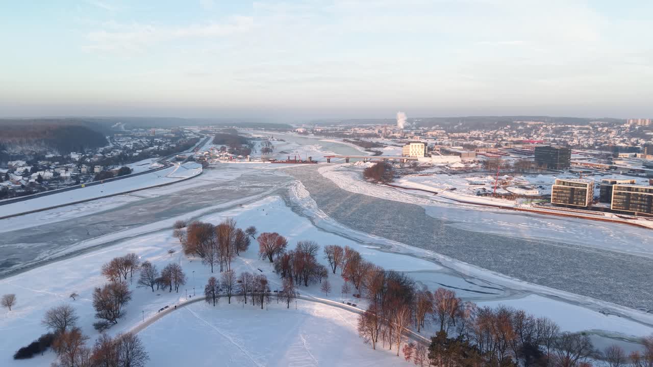 Drone video capturing the serene, snow-covered confluence of the Neris and Nemunas rivers in Kaunas, Lithuania. The landscape is enveloped in winter's embrace, offering a panoramic view