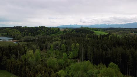 scenic 4k aerial drone flight with view upon bavaria's idyllic lakes in the rural countryside with a beautiful sky and the alps mountains in the background, green lush fields and forest in spring time