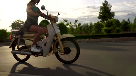 mujer montando en moto sola en la carretera con sol de verano en segundo plano