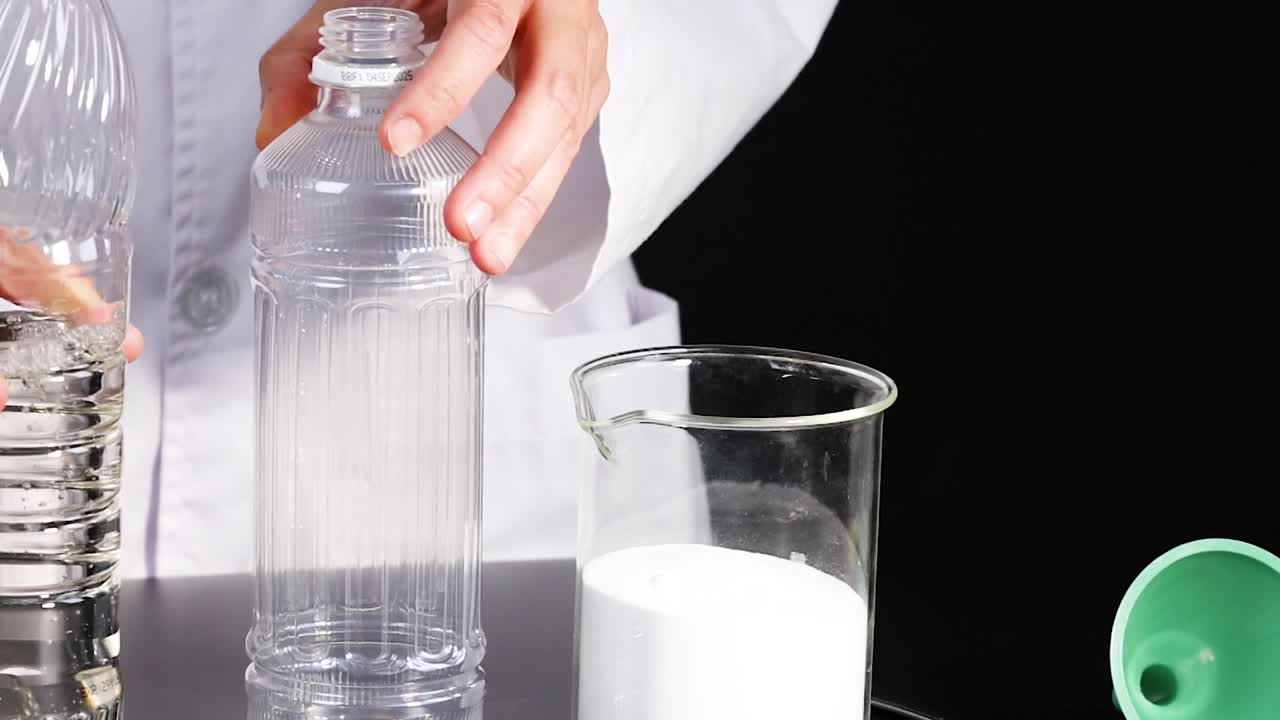 Hands in a lab coat pour liquid from a bottle into another container beside a beaker.