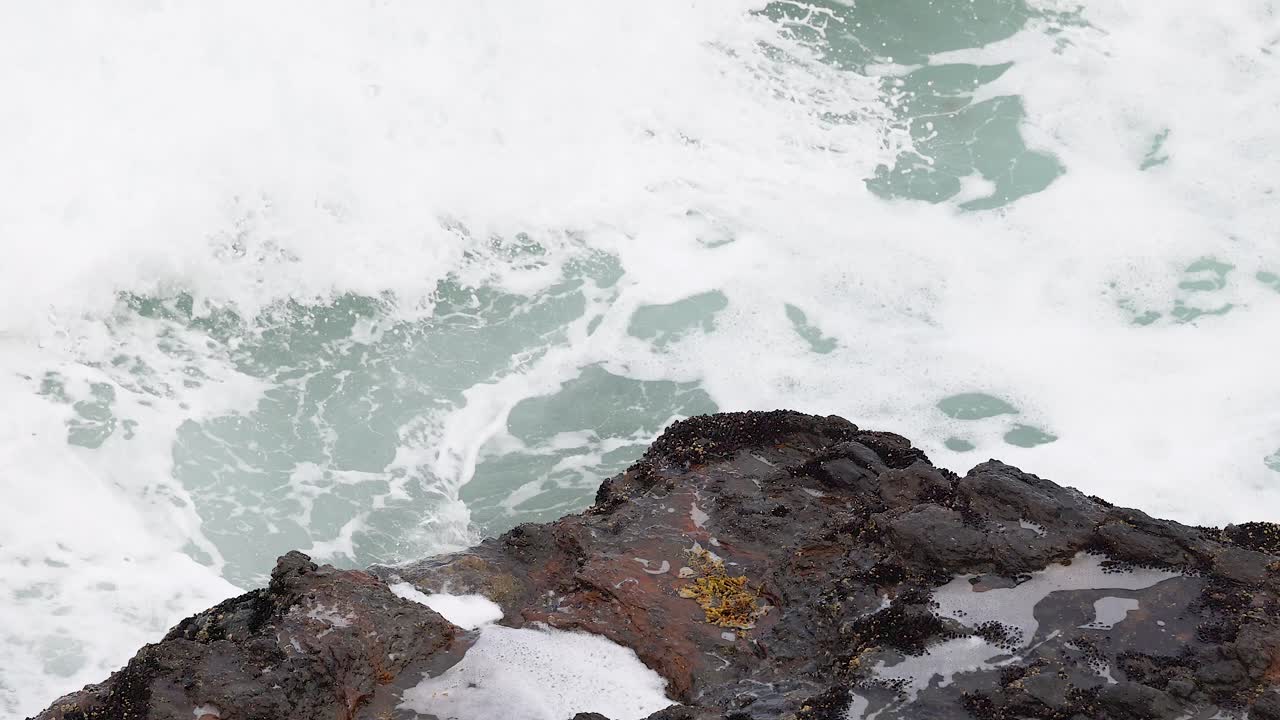 Dynamic ocean waves crash against rugged rocks, captured in bright daylight along Australia's Great Ocean Road