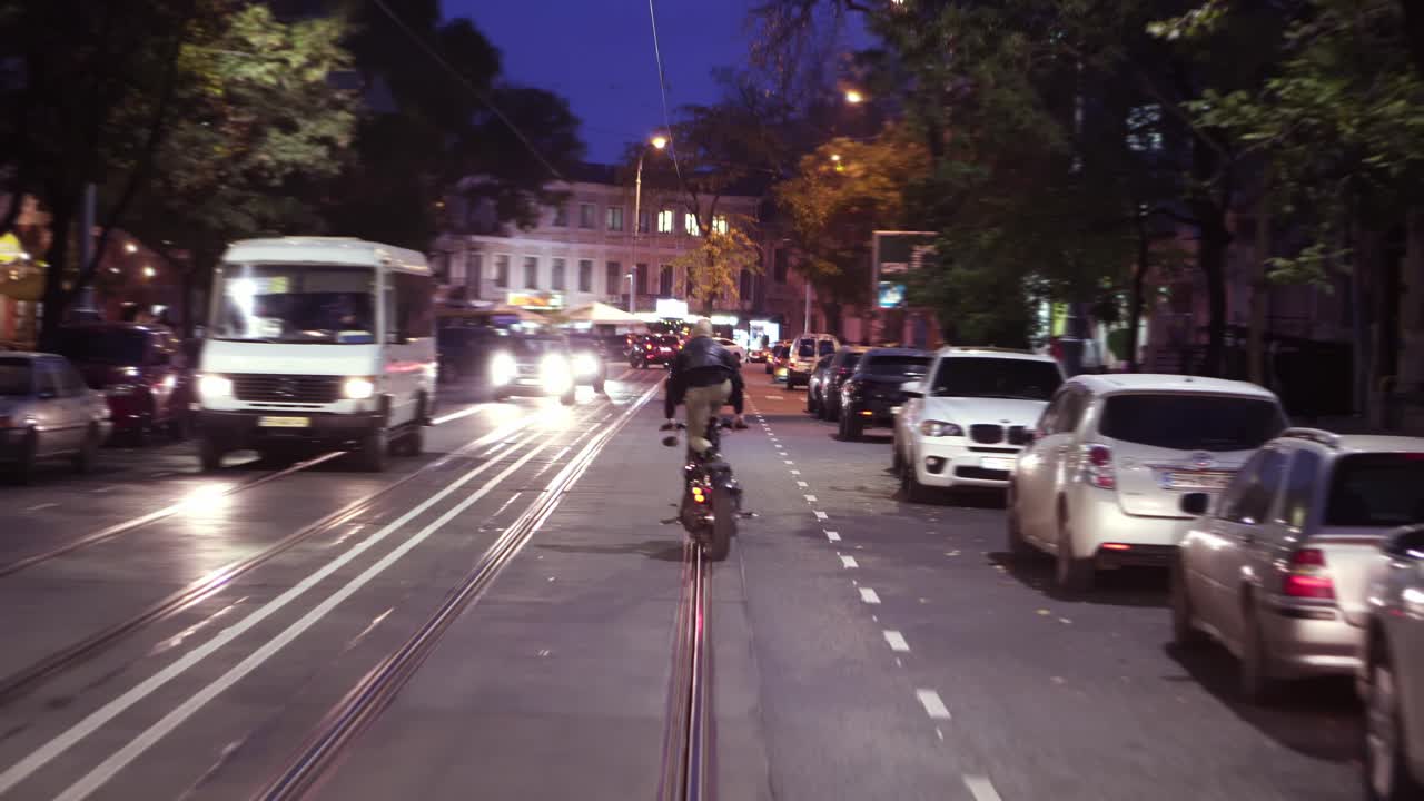 오토바이를 타고 도시에서 스턴트 라이딩을 하는 큰 남자가 밤 도시에서 좌석에 서 있습니다.