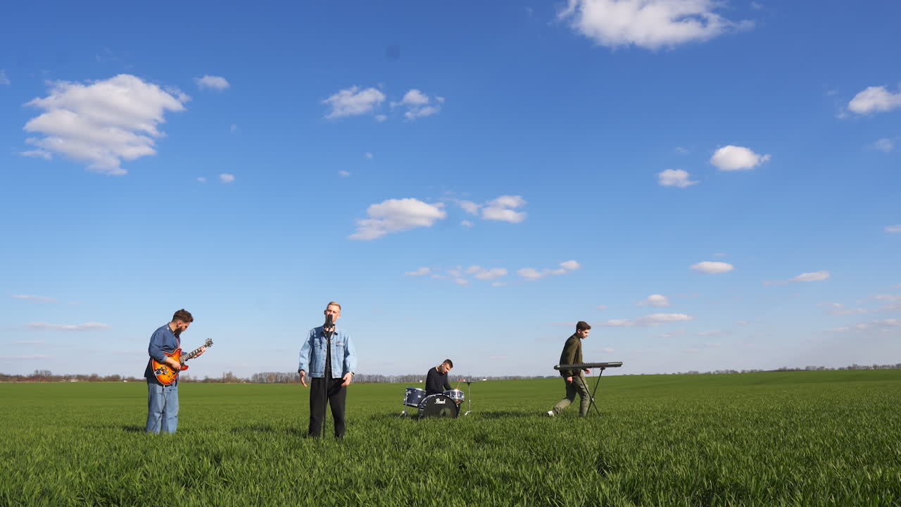 Male music band playing and singing outside the city. Boys' band performing in the green field on sunny day.