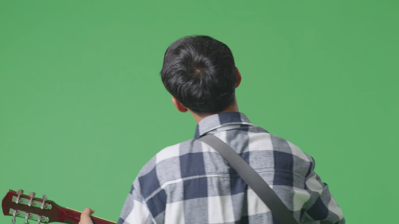 녹색 스크린 배경에 록 음악과 함께 기타를 연주하는 젊은 아시아 십대 소년의 근접적인 뒷면