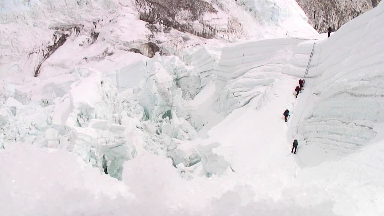 빙폭 꼭대기에 있는 큰 사다리를 타고 올라가는 등반가들