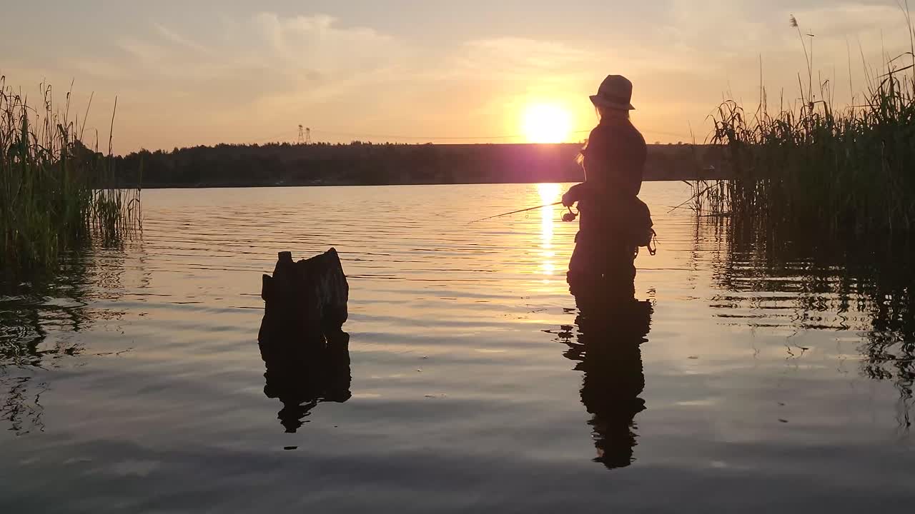 Seorang gadis memancing di danau yang tenang dengan matahari terbenam yang sempurna di kejauhan