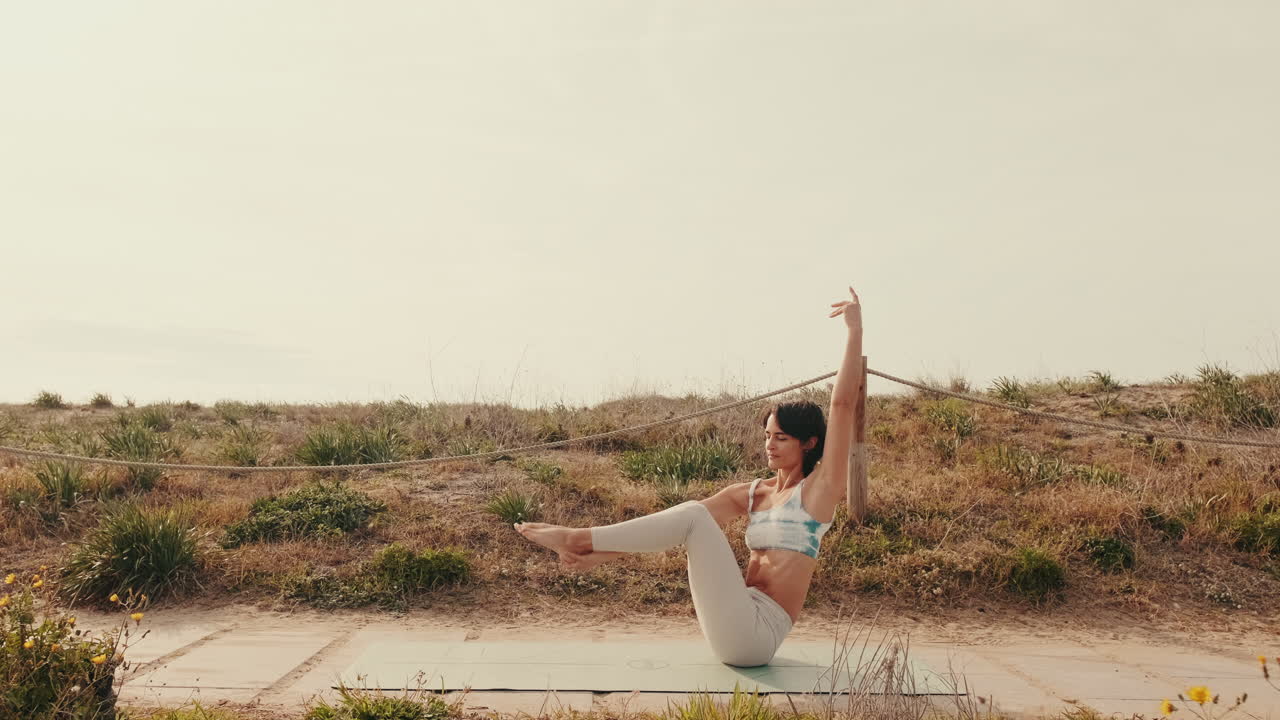 Giovane donna che pratica la posa della barca yoga all'aperto su un tappetino
