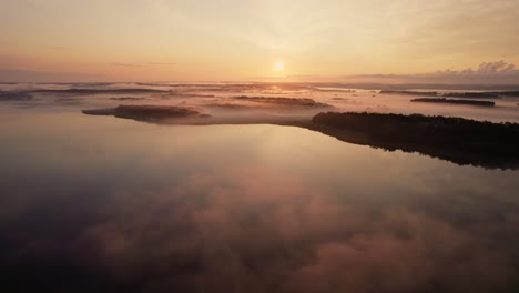 Aerial-drone-view-flying-over-misty-Scandinavian-lake-at-dawn-with-colourful-sunrise,-4k