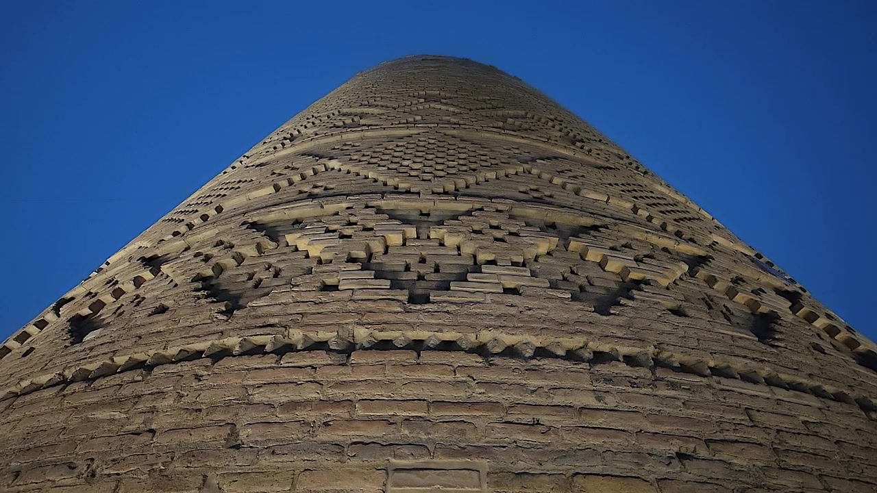 Pohled zdola na starobylý cihlový minaret proti jasně modré obloze.