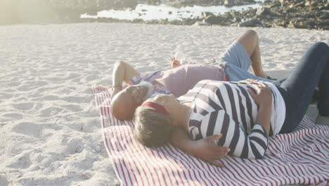 happy senior african american couple lying on blanket at beach, slow motion