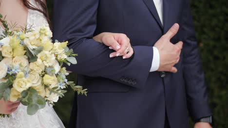 bride and groom holding hands during outside garden wedding ceremony close up shot, with flowers and bouquet in her hands