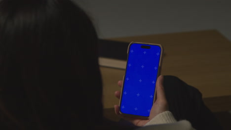 Over The Shoulder Shot Of Woman At Home Sitting On Sofa With Blue Screen Mobile Phone Scrolling Through Internet Or Social Media 2
