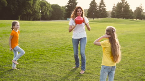 Glückliche-Mutter-Und-Ihre-Zwei-Kleinen-Töchter-Spielen-Mit-Ball-Auf-Wiese-1