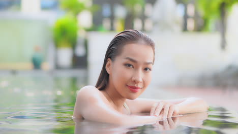 medium close-up, a pretty young woman leaning on her arms against the infinity edge of a resort pool turns her head toward the camera