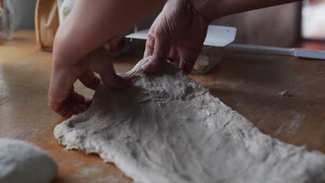 fresh dough stretched by hand over on wooden tabletop, filmed in close up handheld slow motion style