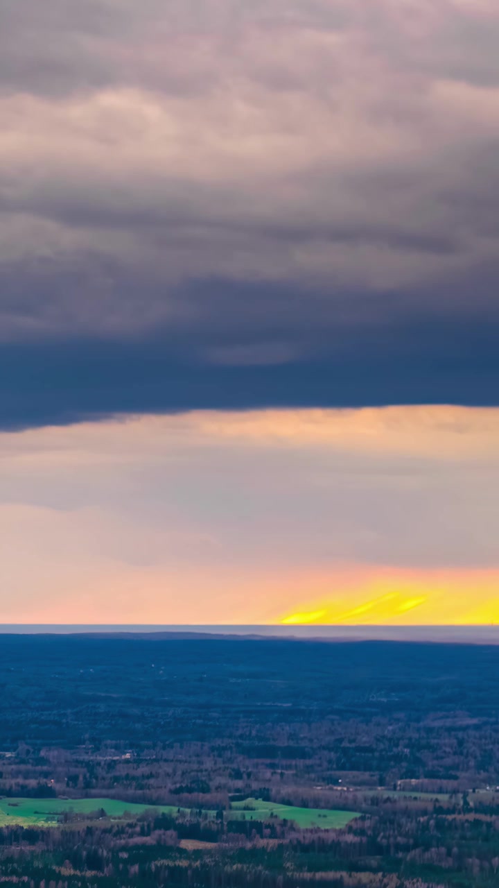 Timelapse captures dark storm clouds moving across sky above rural farmland as golden sunset light breaks through horizon