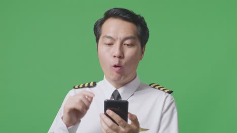 close up of asian man pilot looking at smartphone, smiling, and saying wow while standing in the green screen background studio