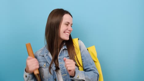 joven estudiante adolescente sonriente alegre sostener libros descanso de baile, lleva chaqueta de denim y mochila amarilla, posando aislado sobre fondo de color azul estudio. educación en la escuela secundaria concepto de universidad universidad