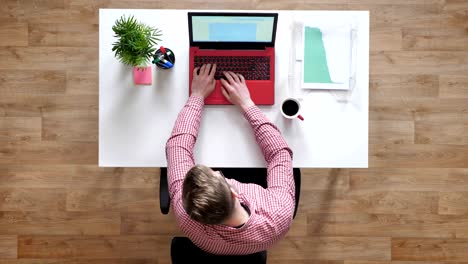 young man in glasses working on laptop, speaking on phone and taking documents, busy, topshot, sitting behind desk