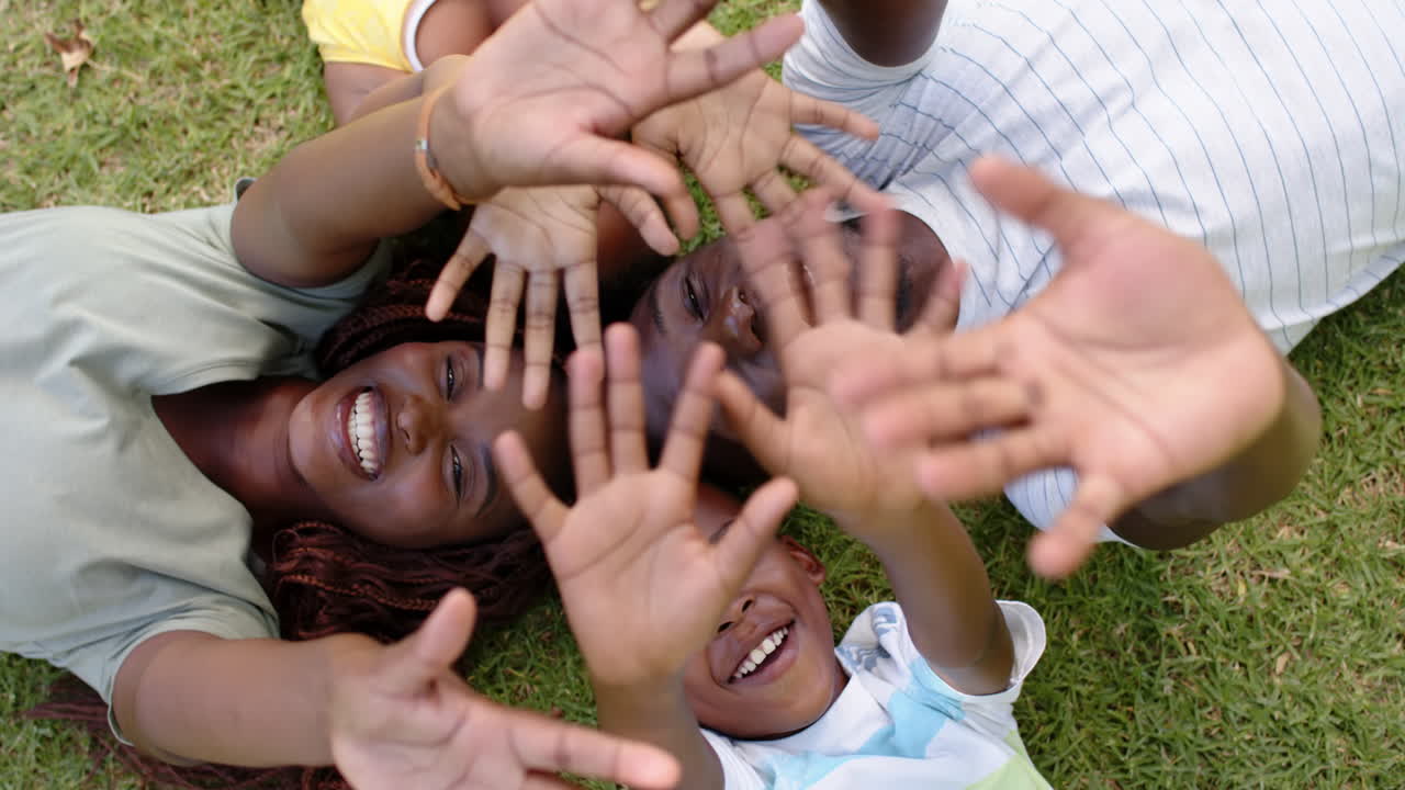 Smiling african american family lying on grass, reaching hands towards camera, enjoying outdoor time