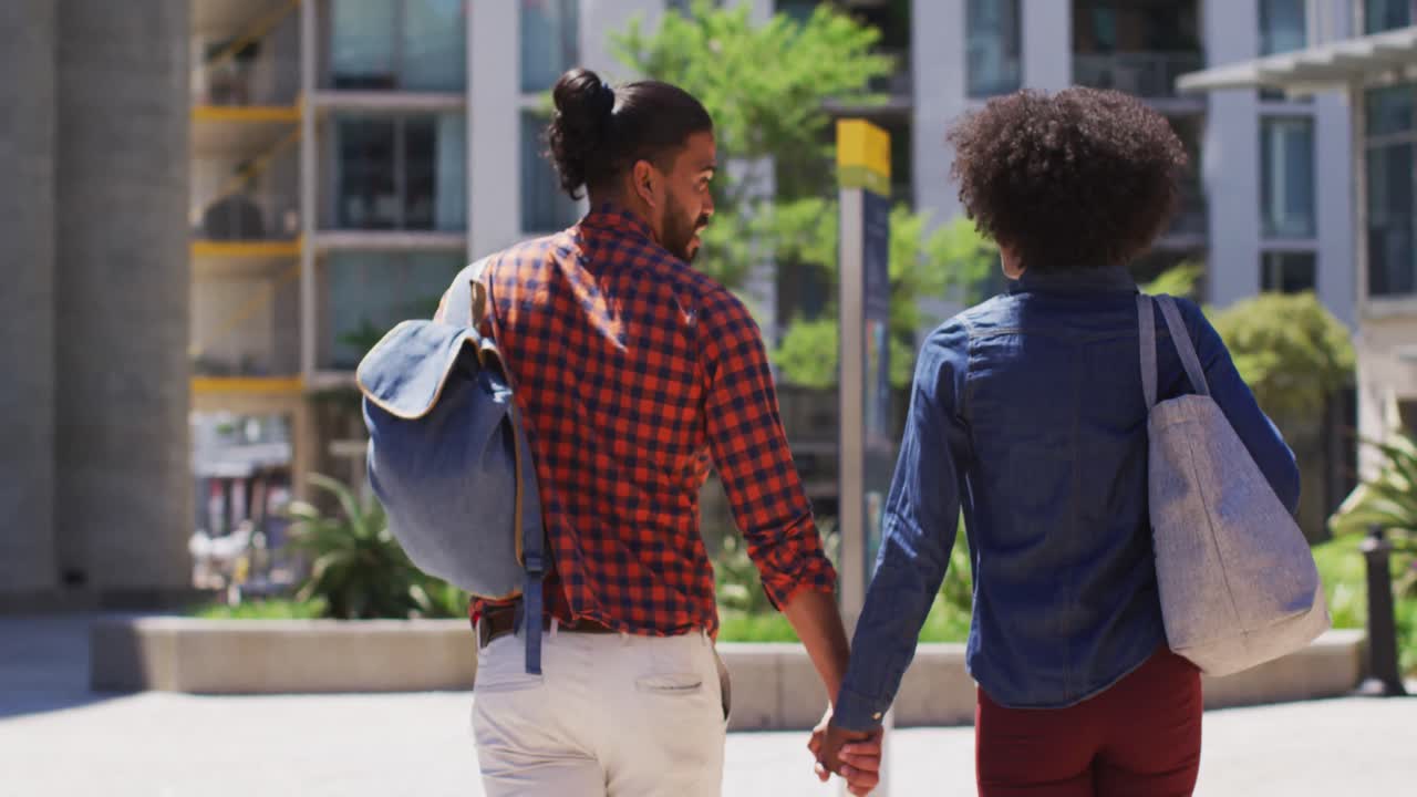 pareja diversa caminando por la calle tomados de la mano sonriendo y hablando
