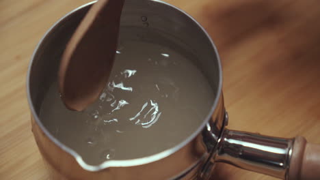 Woman-stirring-water-in-a-metal-pan-with-a-wooden-spoon