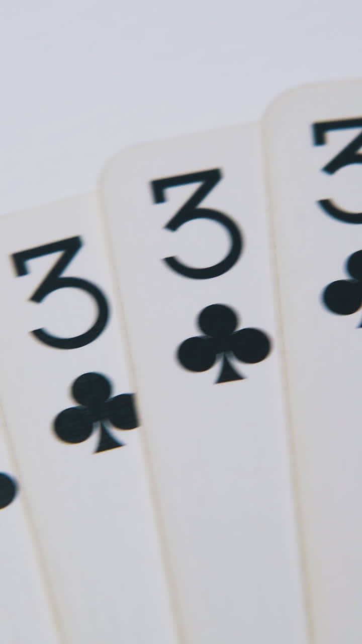 Movimento sopra un ventaglio di carte da gioco nere a fiori, giacenti su una superficie bianca pulita, primo piano estremo.