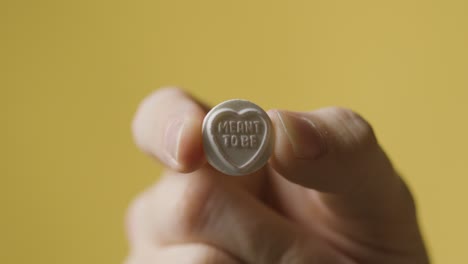 close up of hand holding heart candy avec censé être un message sur fond jaune