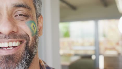 happy biracial man with flag of brazil on cheek at home