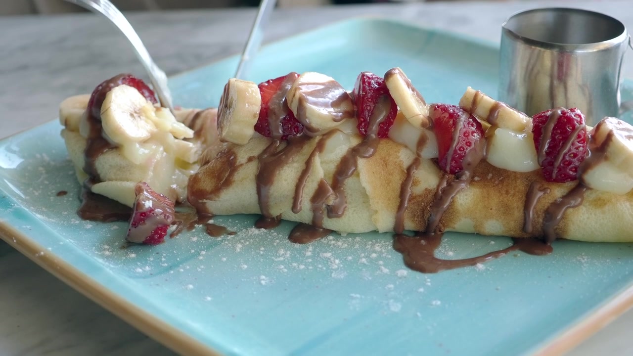 Persona che taglia una deliziosa crepe con fragole e banane.