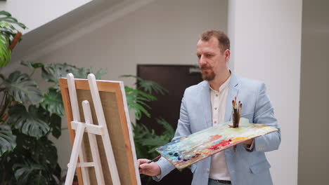 artist creates drawing with oil paints in studio. serious man applies different paints smears onto canvas in workshop. artistic hobby to improve mood