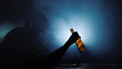 Silhouette-of-a-man-sitting-with-an-empty-bottle-of-alcohol-in-his-hand