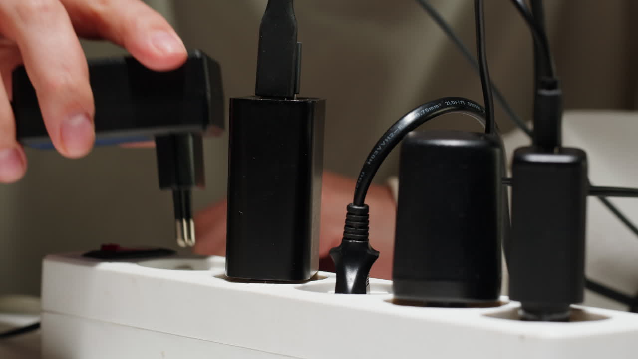 White power strip with many various of cords and cables in close-up. An extension cord with many power sockets. Adapter with phone, headphones, usb connectors.Tangled wires on table. Trying to untangle many messy cables.