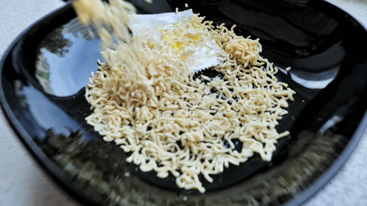 La visualizzazione ravvicinata mostra degli spaghetti istantanei versati in una ciotola nera prima della preparazione