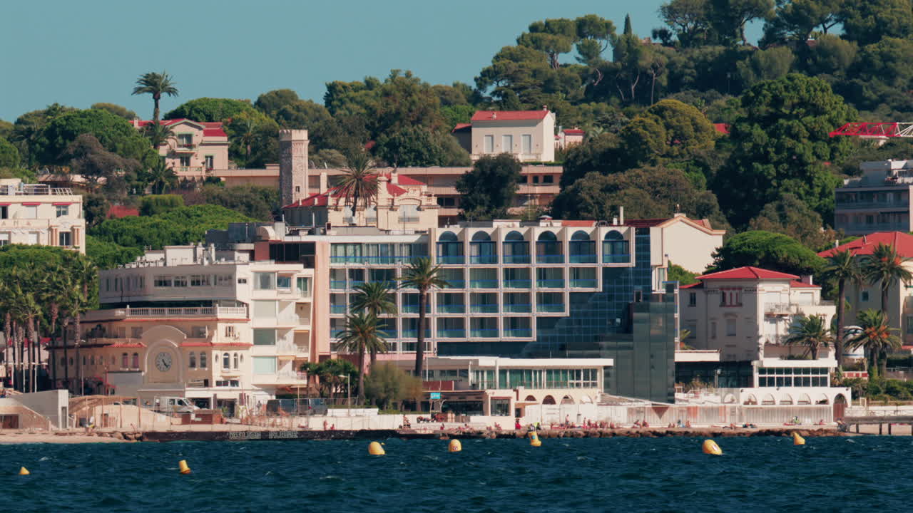 Scenic view of coastal architecture and lighthouse surrounded by trees and hills in Cannes, France