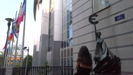 a woman stands before a statue holding the euro sign near the eu parliament.