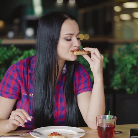 beautiful girl in a plaid shirt is eating a slice of pizza at a table in the pizzeria