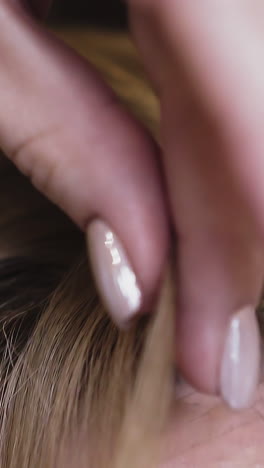 cu, slow motion: young blonde woman with stylish beige manicure touches hair to adjust forehead locks of modern hairstyle in light room extreme close view