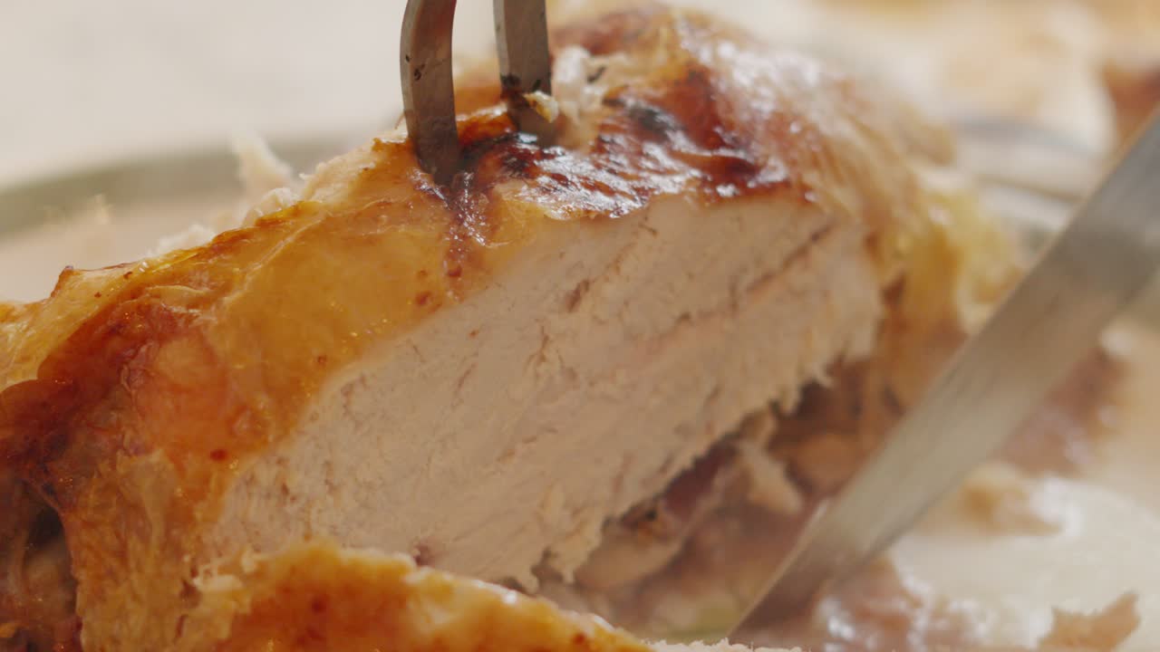 Carving Roast Chicken with Long Fork and Sharp Knife as Pieces are Cut Off to Serve at Sunday Lunch Dinner. Traditional British Poultry Food.