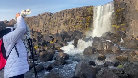 una linda chica rubia se pone una bufanda en la cascada de oxararfoss en un día soleado, islandia
